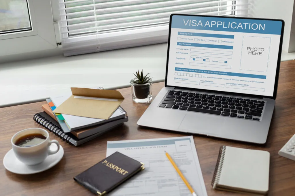 Laptop displaying a visa application form, passport, and paperwork. Immigration lawyer services.
