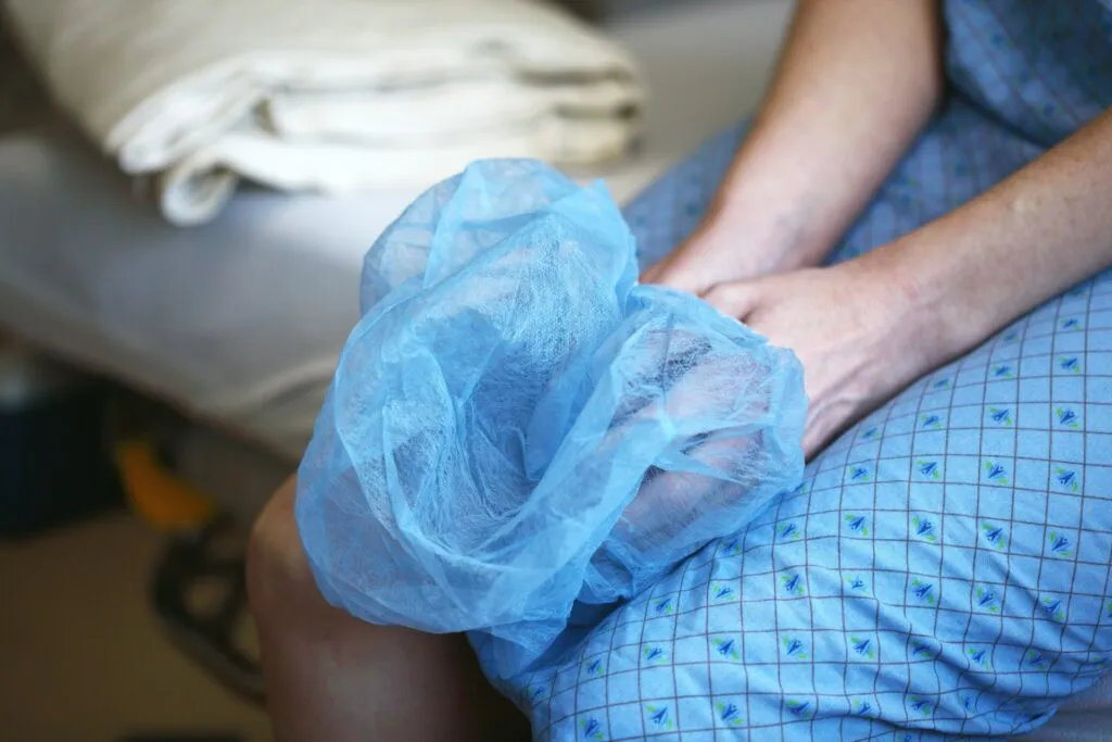 Person in hospital gown holding a blue surgical cap, awaiting medical procedure.