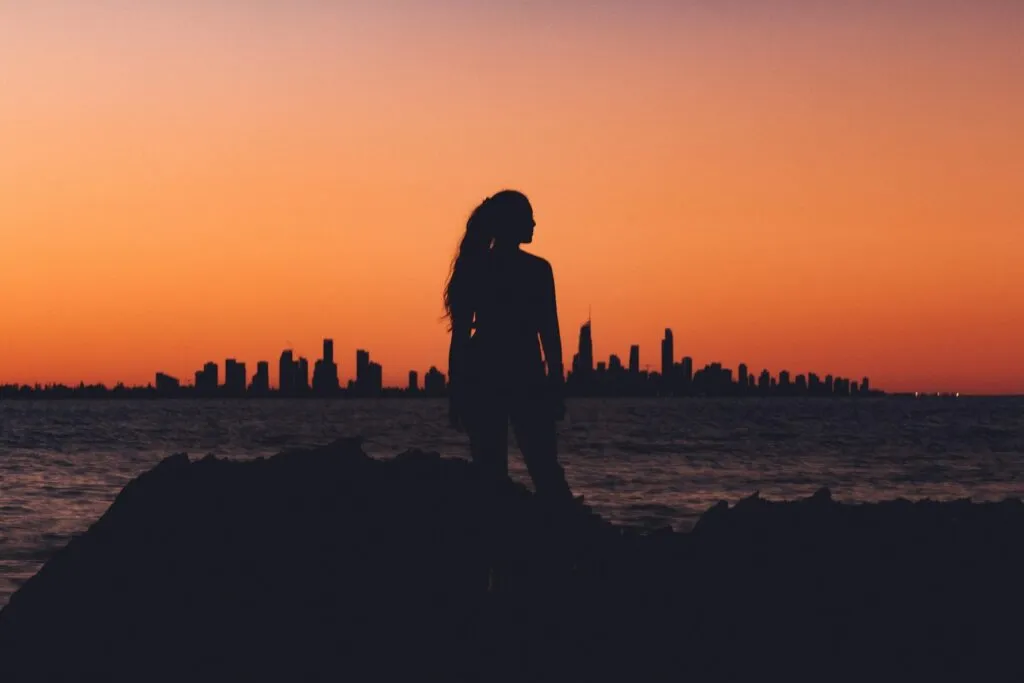 Silhouette of a woman at sunset, city skyline in the background.
