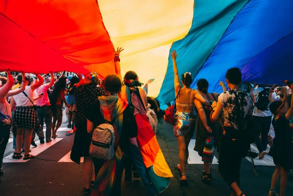 LGBTQ+ Pride parade participants carrying a large rainbow flag.