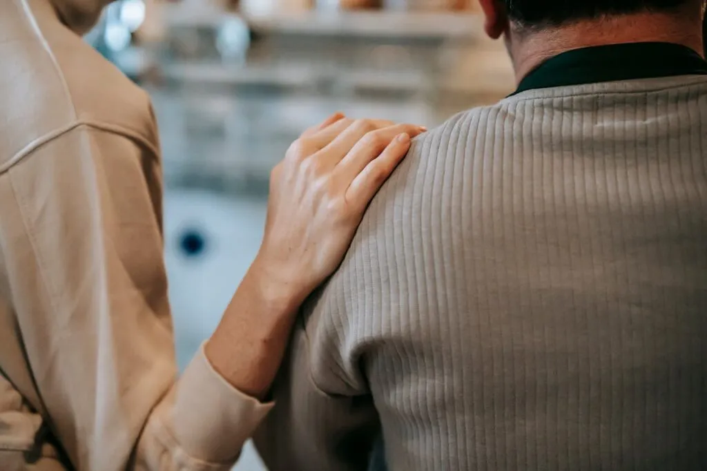 A person comforting another with a hand on their shoulder.