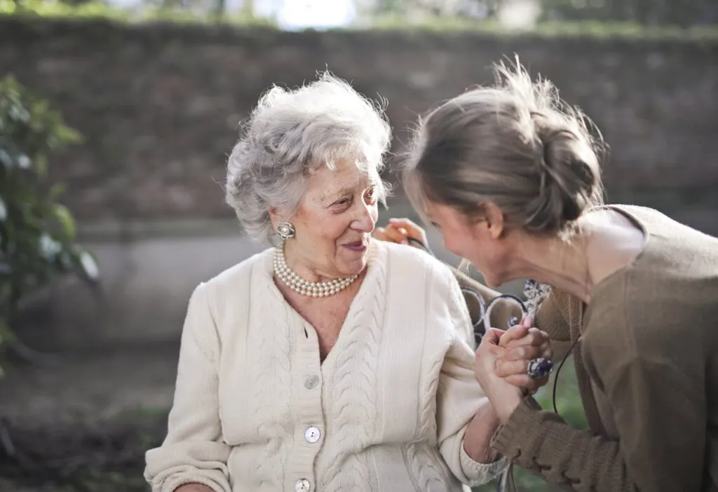 Happy elderly woman and her caregiver holding hands. Supporting family through the Aged Dependent Relative visa process.