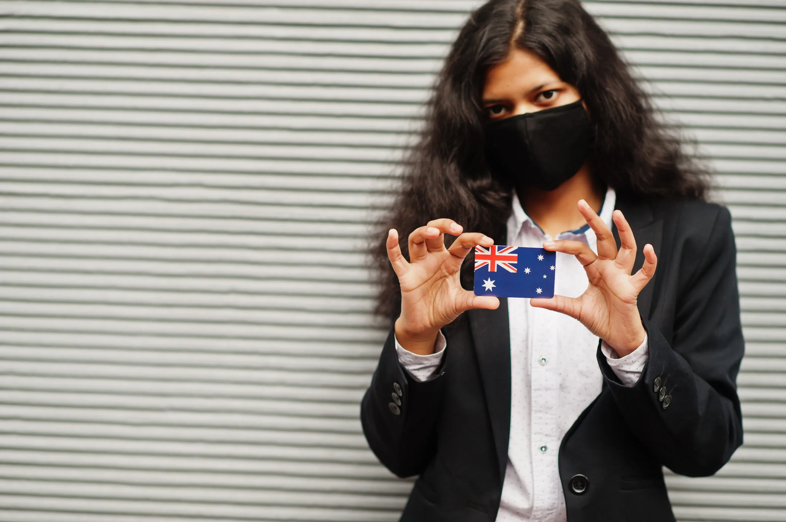 Woman in mask holding Australian flag card. Applying for Australian Citizenship.