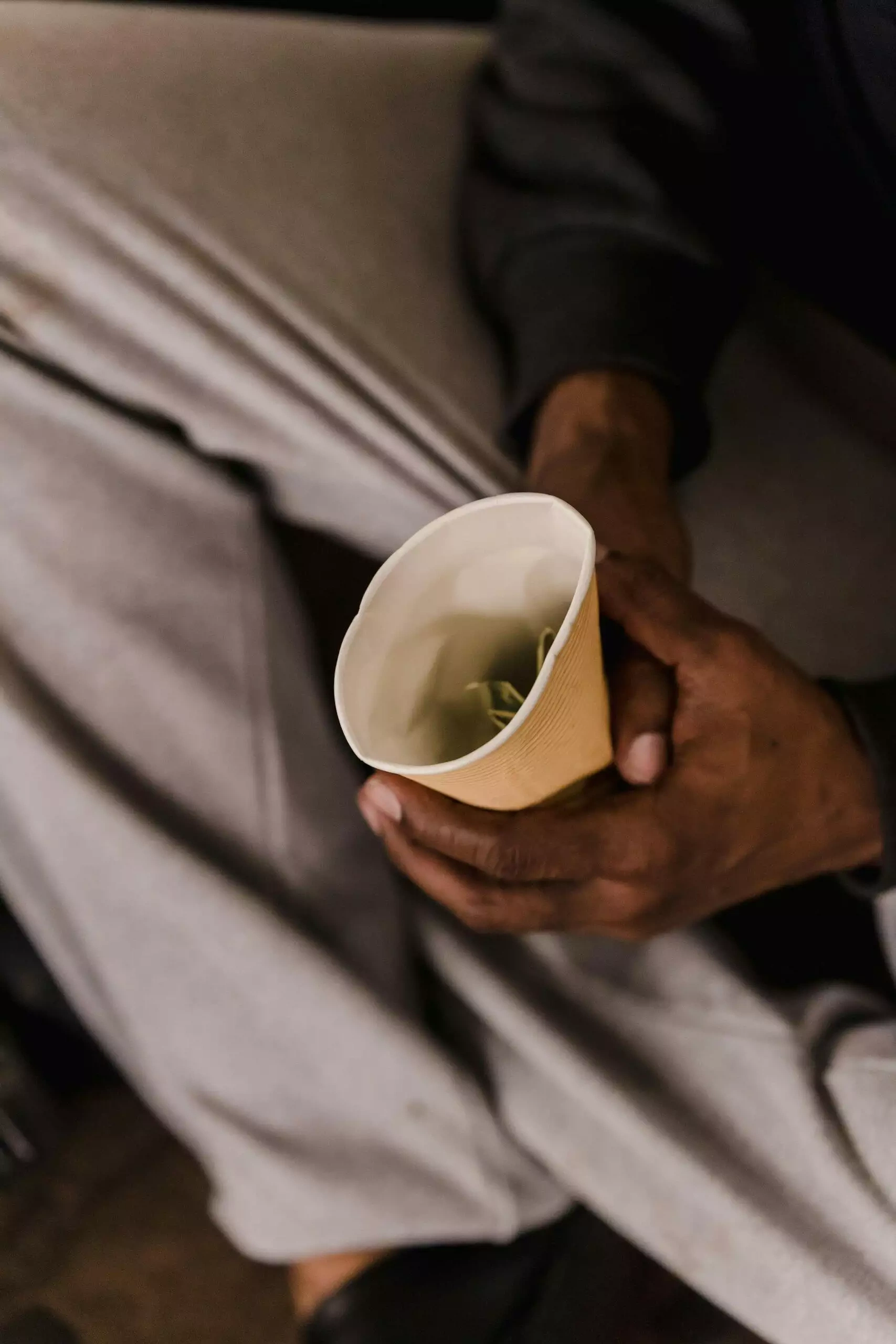 Close-up of hands holding a small paper cup with money inside.