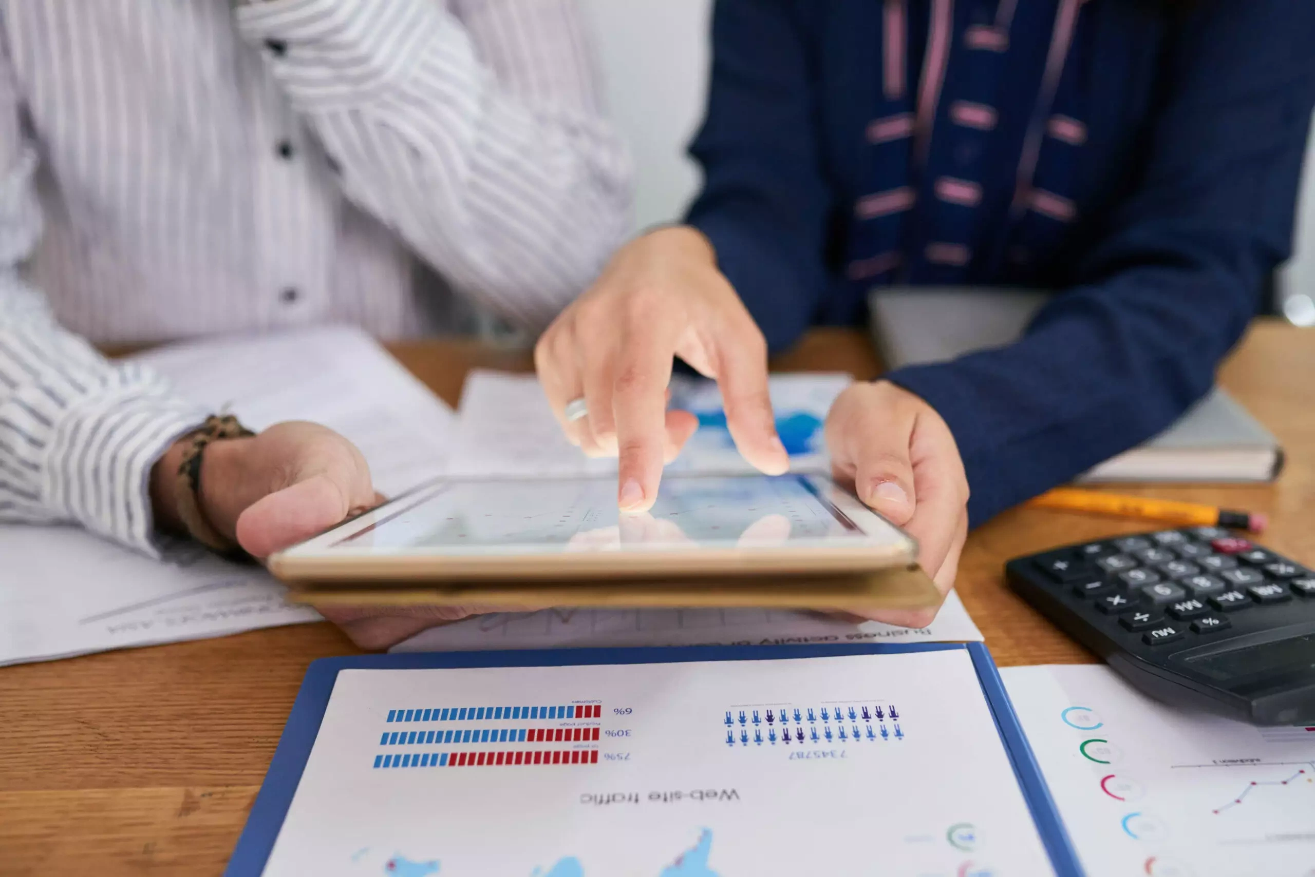 Two people reviewing financial reports on a tablet with printed charts nearby