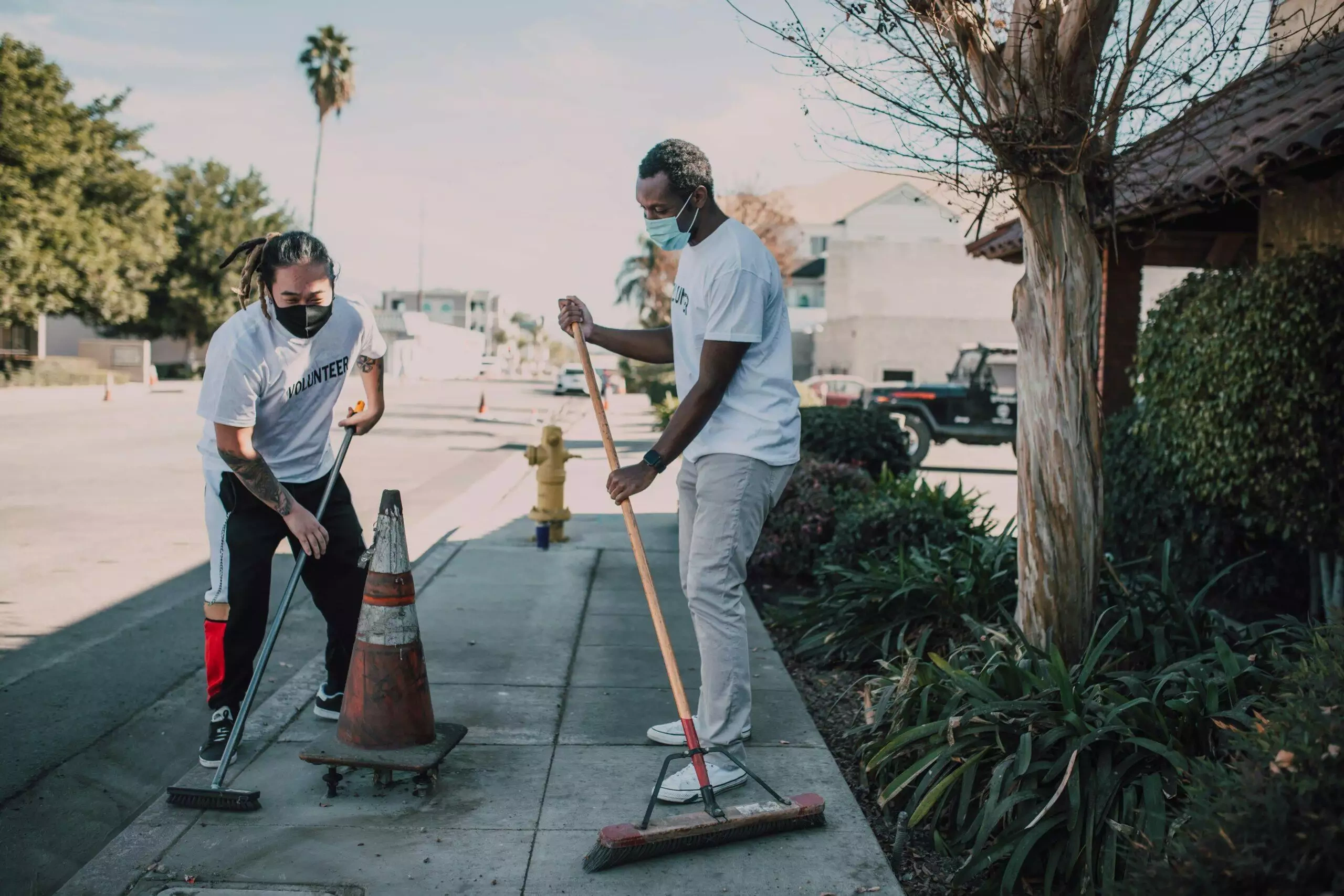 Two masked volunteers sweep a city street, demonstrating community service and civic engagement.