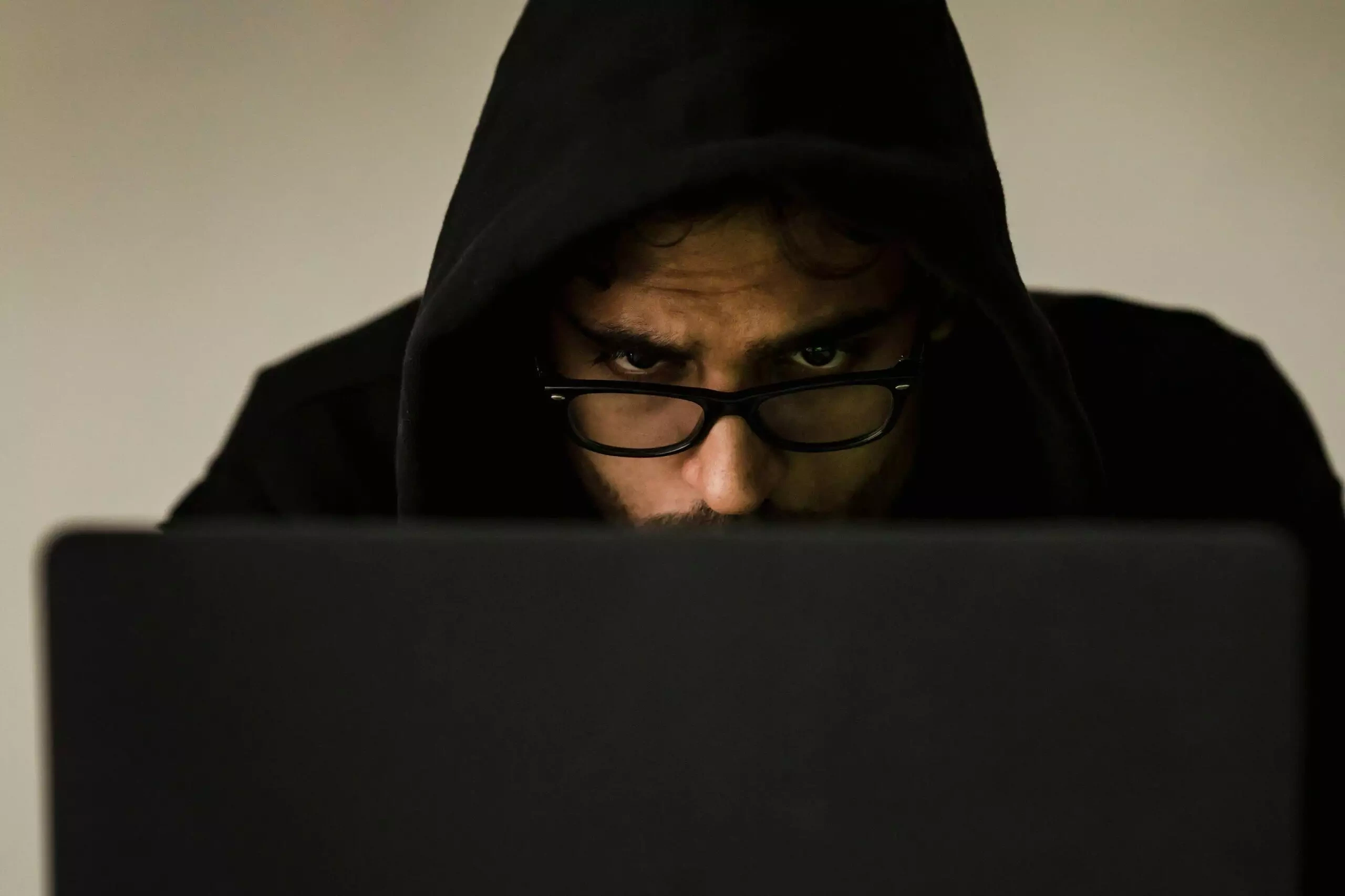 A man in a hooded sweatshirt looks intently at a laptop screen. His focus suggests serious work.