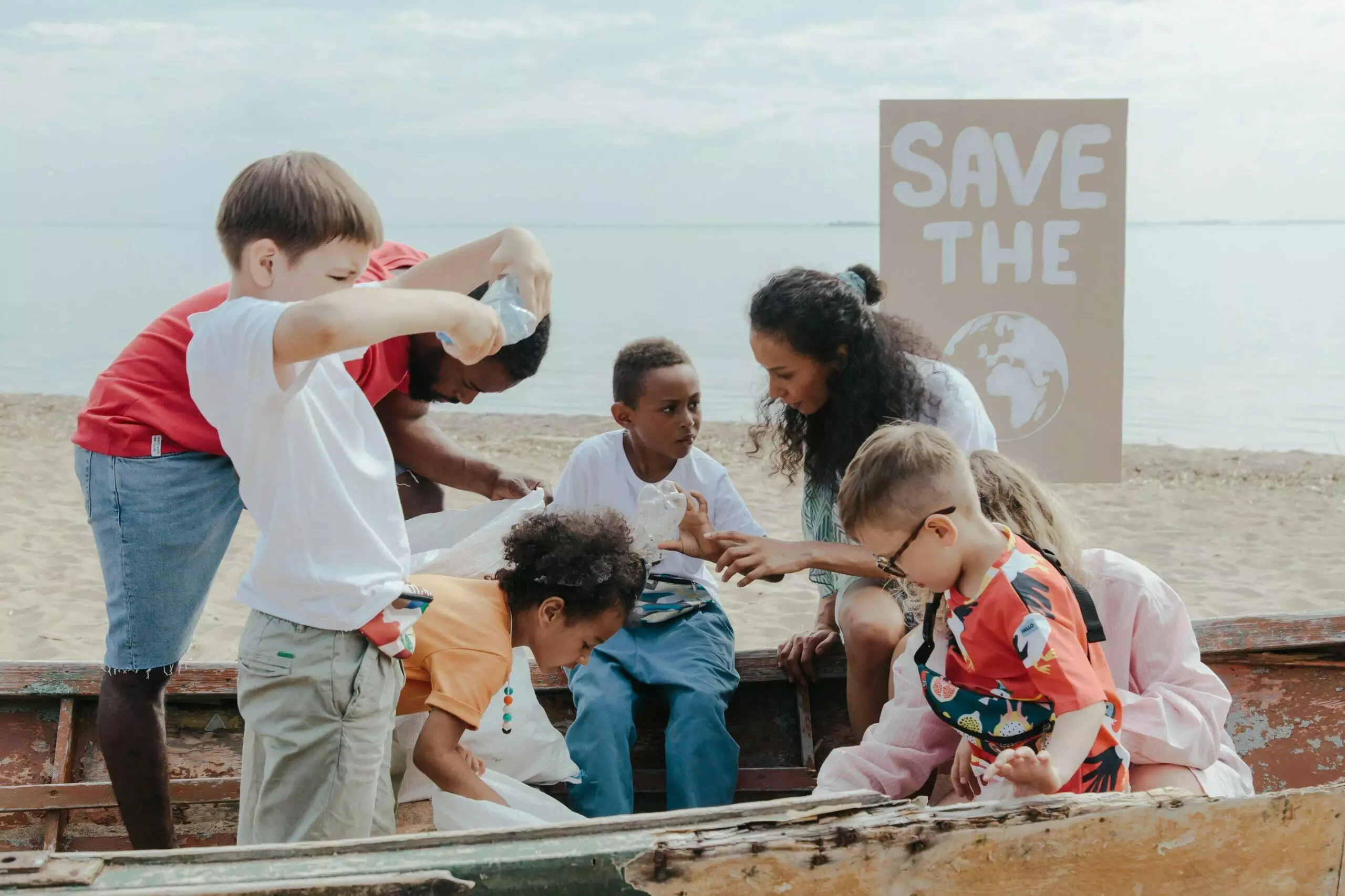 Children and adults collect plastic waste from a boat on a beach, with a 