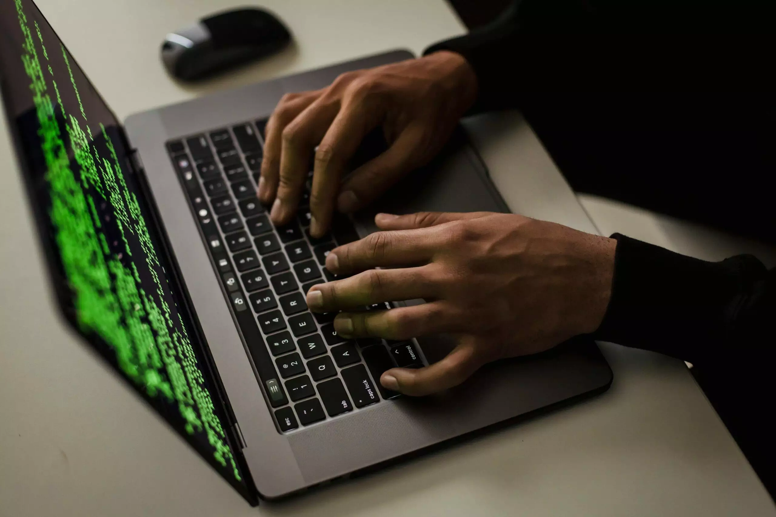Person's hands typing code on a laptop, green text visible on the screen.