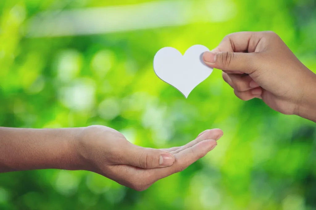 Hands exchanging a paper heart; symbolizing charitable giving.