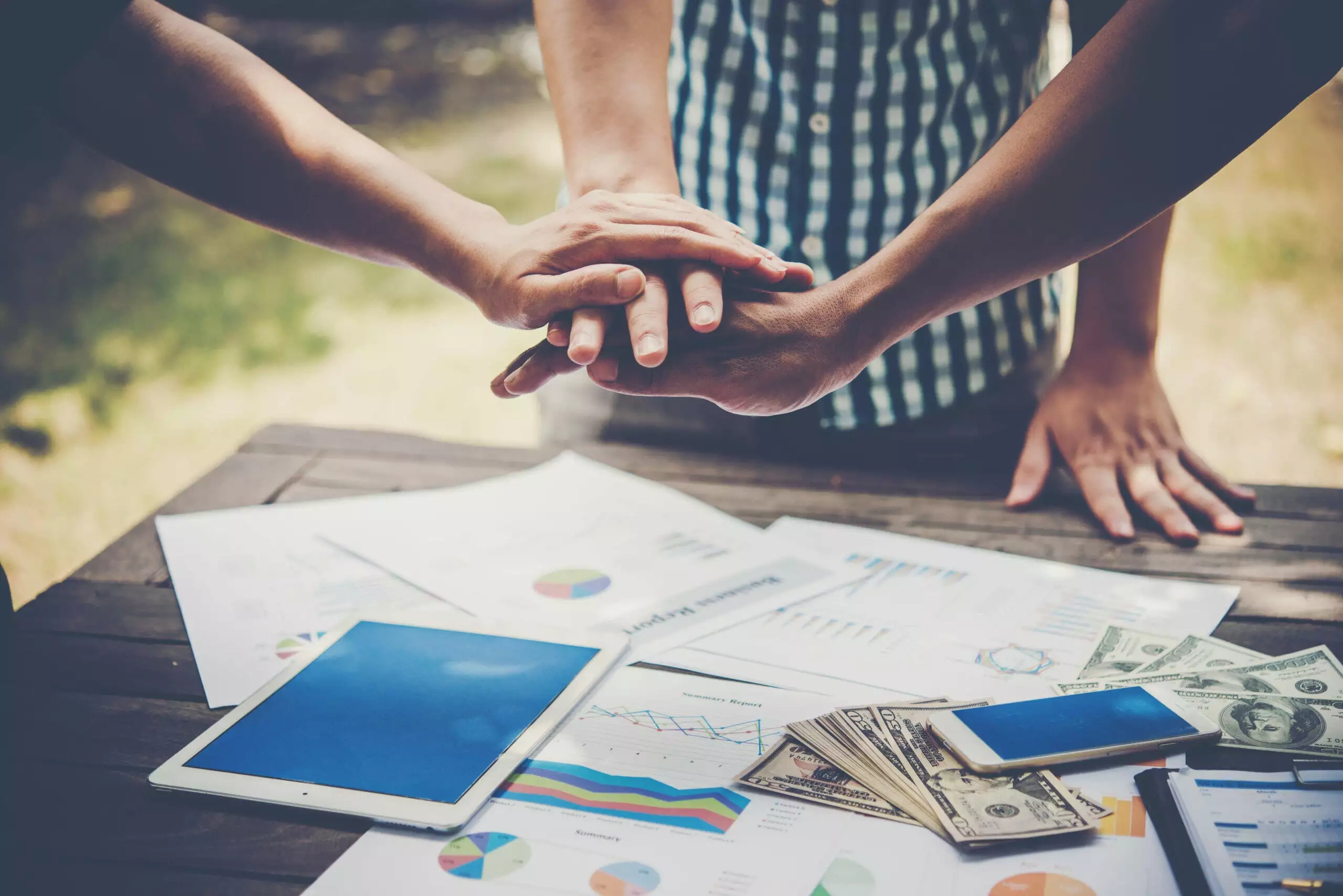 Team members stacking hands over financial documents and tablets on a table