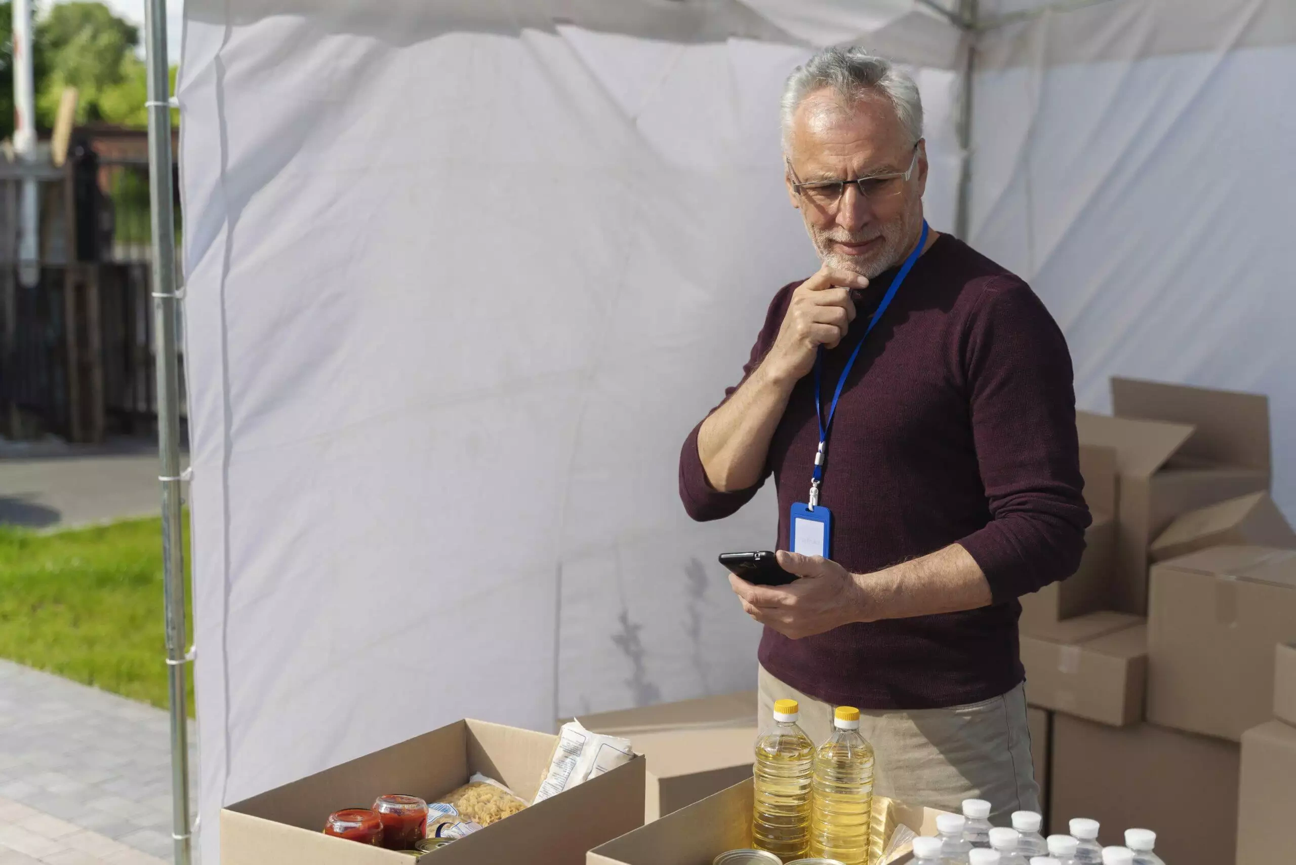 Senior volunteer at a food bank checks inventory on his phone, ensuring ACNC compliance.