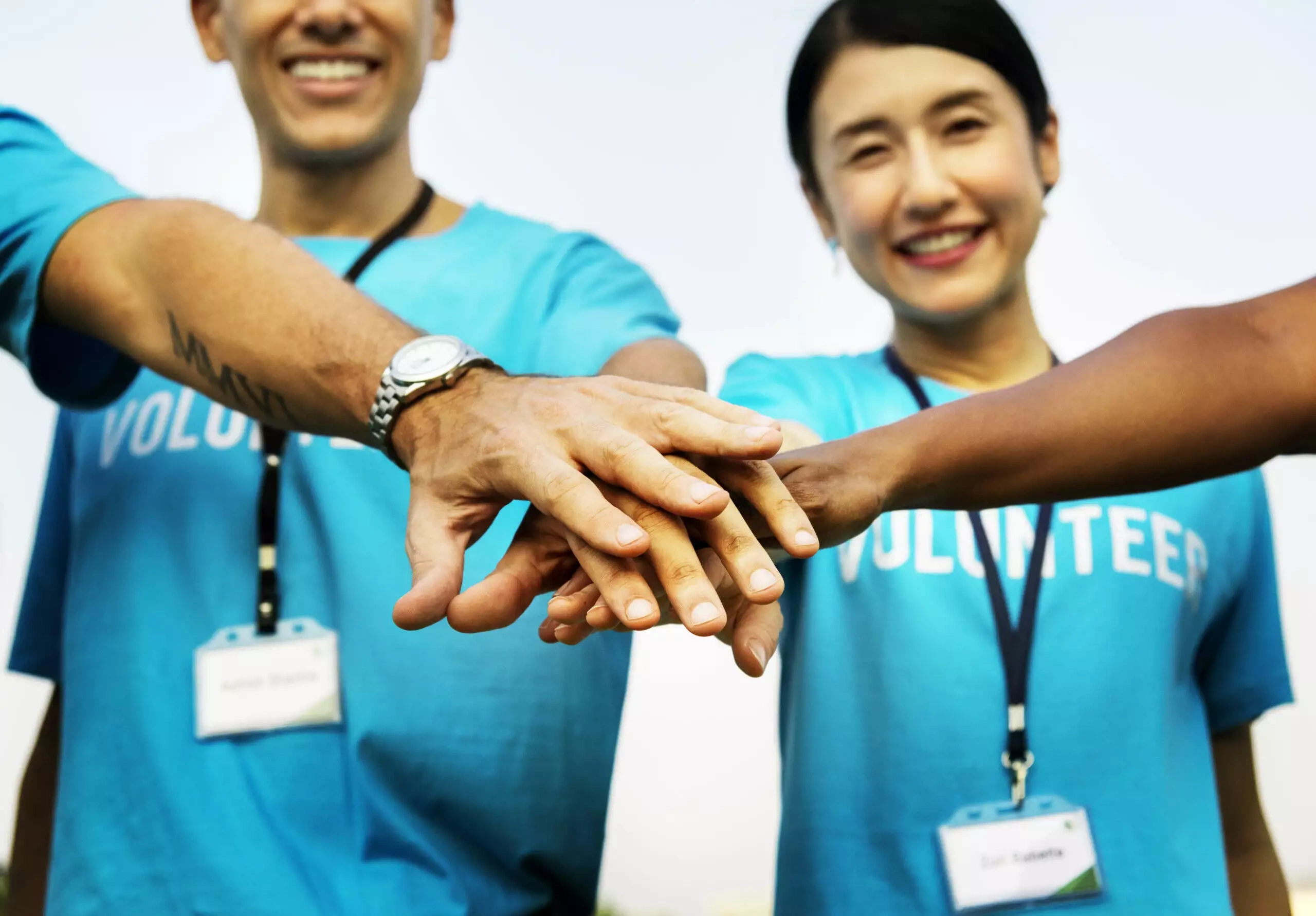 Smiling volunteers in blue shirts stack hands in unity
