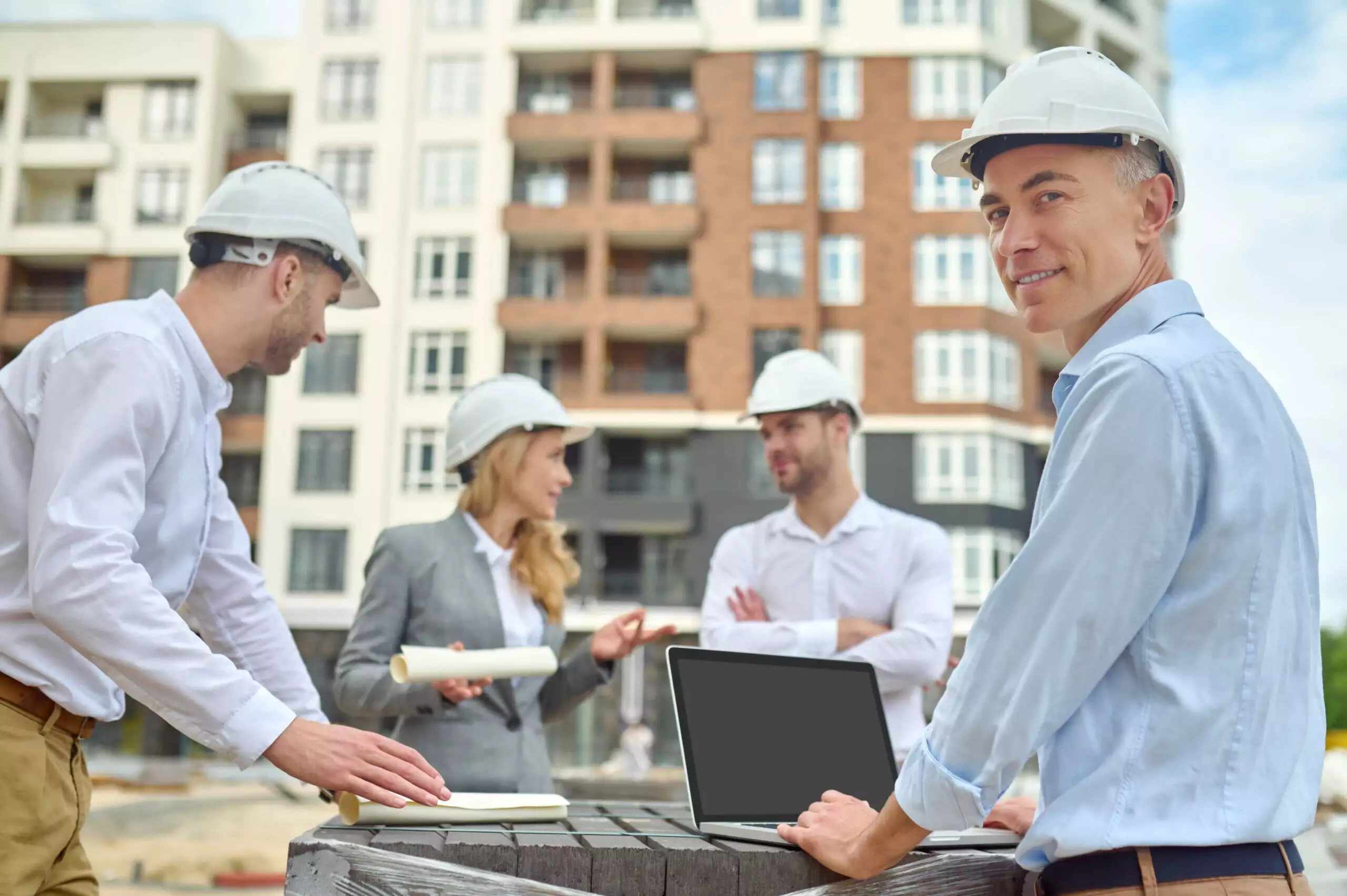 Construction team with a laptop discussing developments in front of a building site
