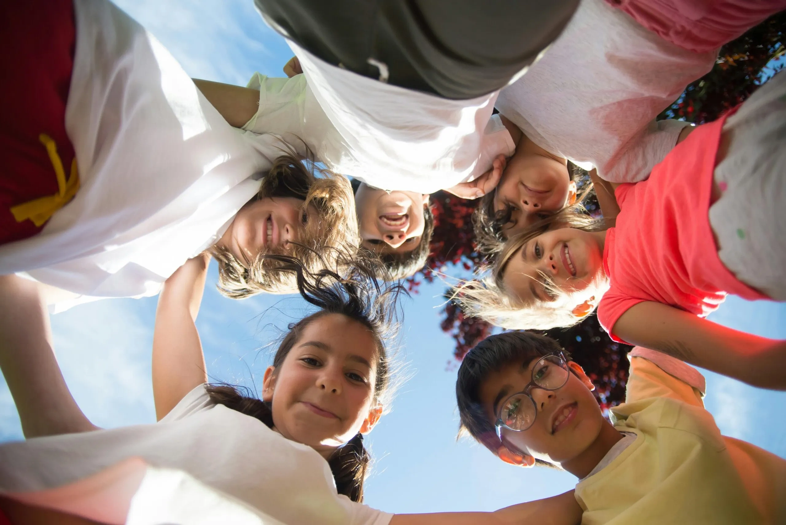 Children in a huddle looking down at the camera, smiling. Friendship and togetherness.