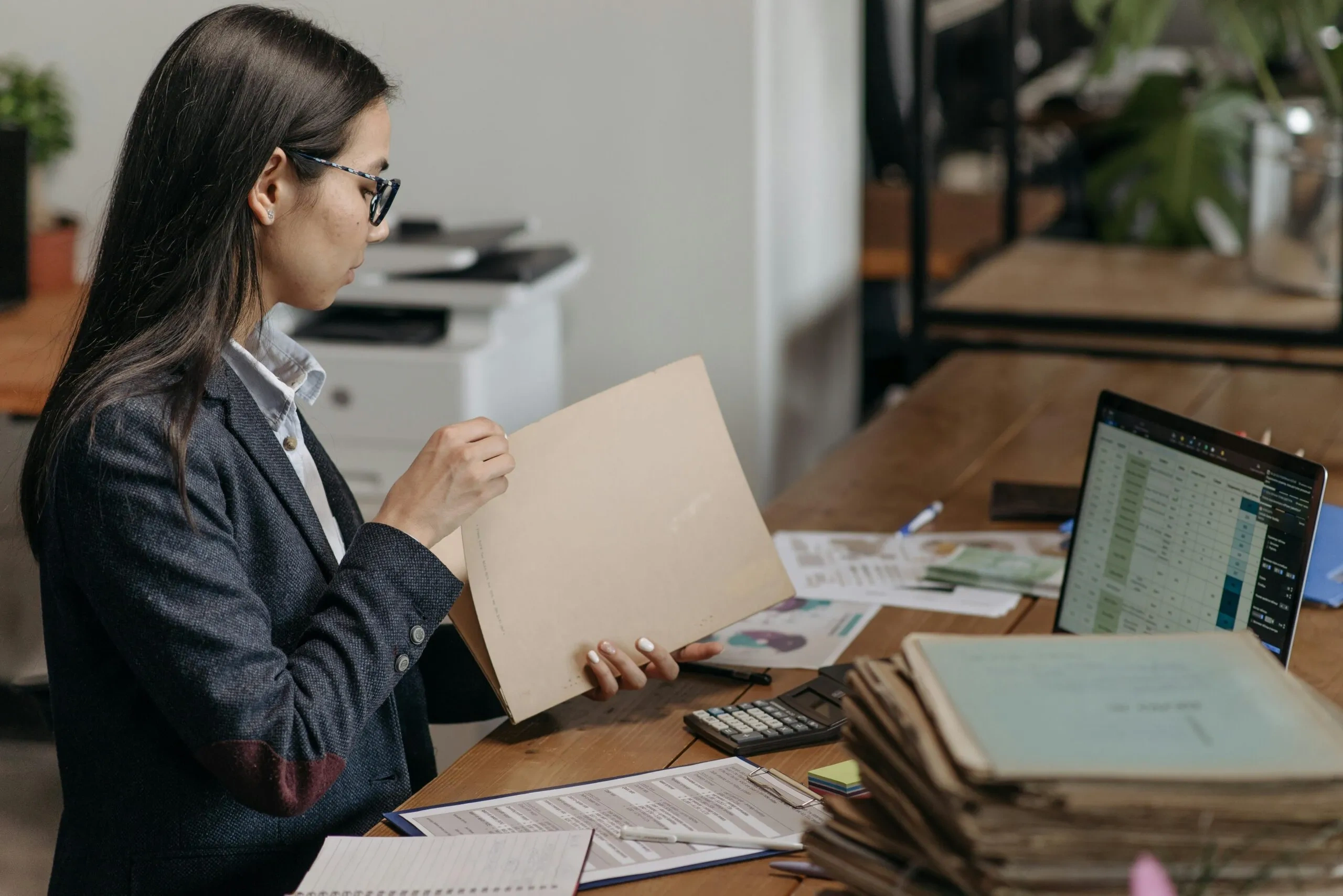 Woman reviewing documents at a desk. Laptop, calculator, and paperwork visible for NSW conveyancing tasks.