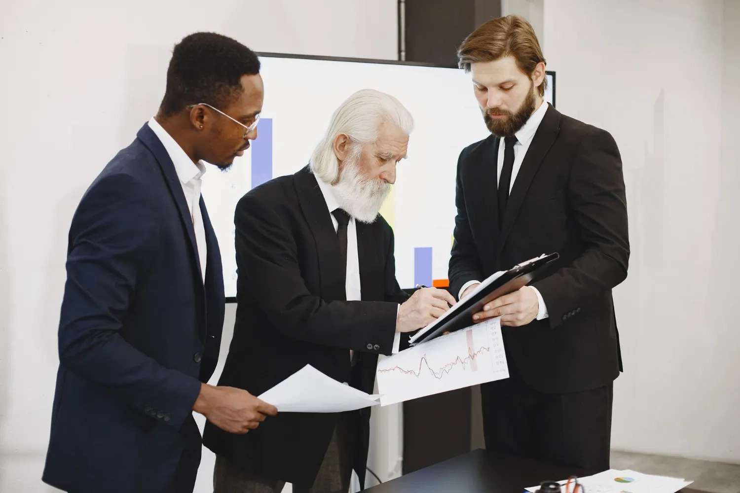 Three business professionals reviewing financial charts and documents at a meeting.