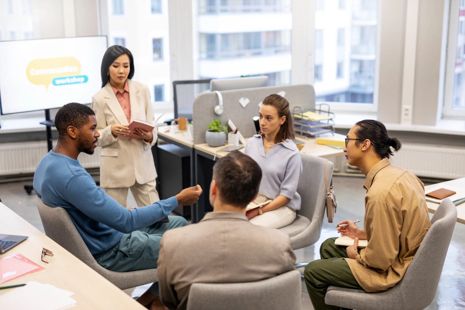 Group at a conversation workshop, led by an Asian woman in a suit. 