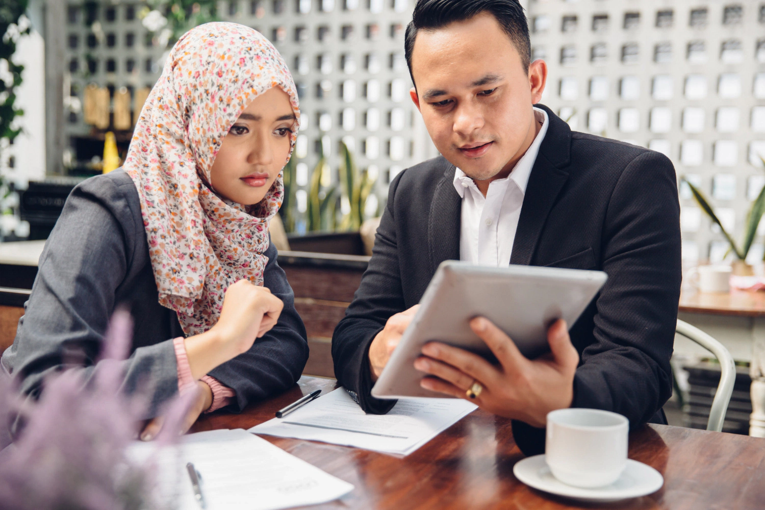 Muslim business partners review Islamic SMSF documents on a tablet at a cafe.