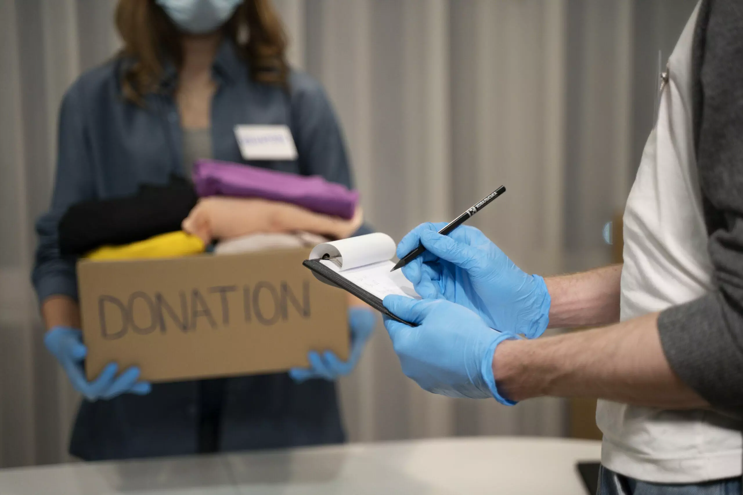 Person holding a donation box with clothes while another writes on a clipboard
