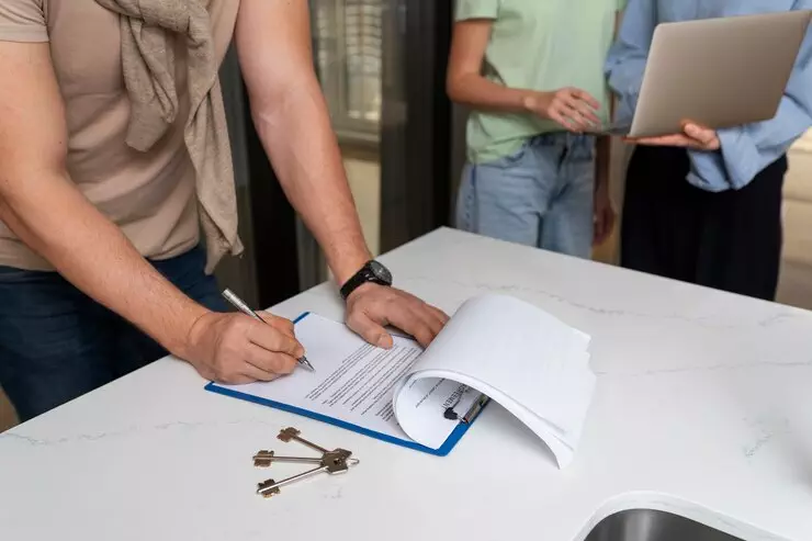Person signing NSW off-the-plan contract documents. Keys on table.