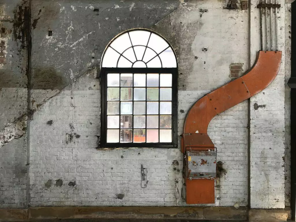 Aged brick wall with arched window and industrial ventilation duct.