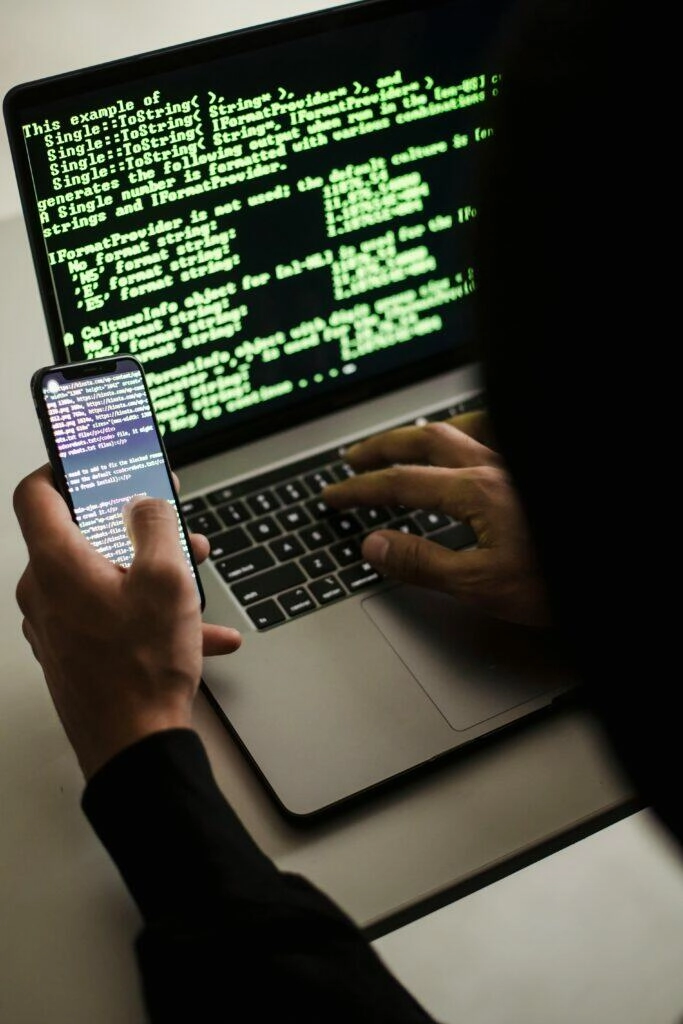 Person working on laptop and phone, reviewing code to protect against charity fraud.