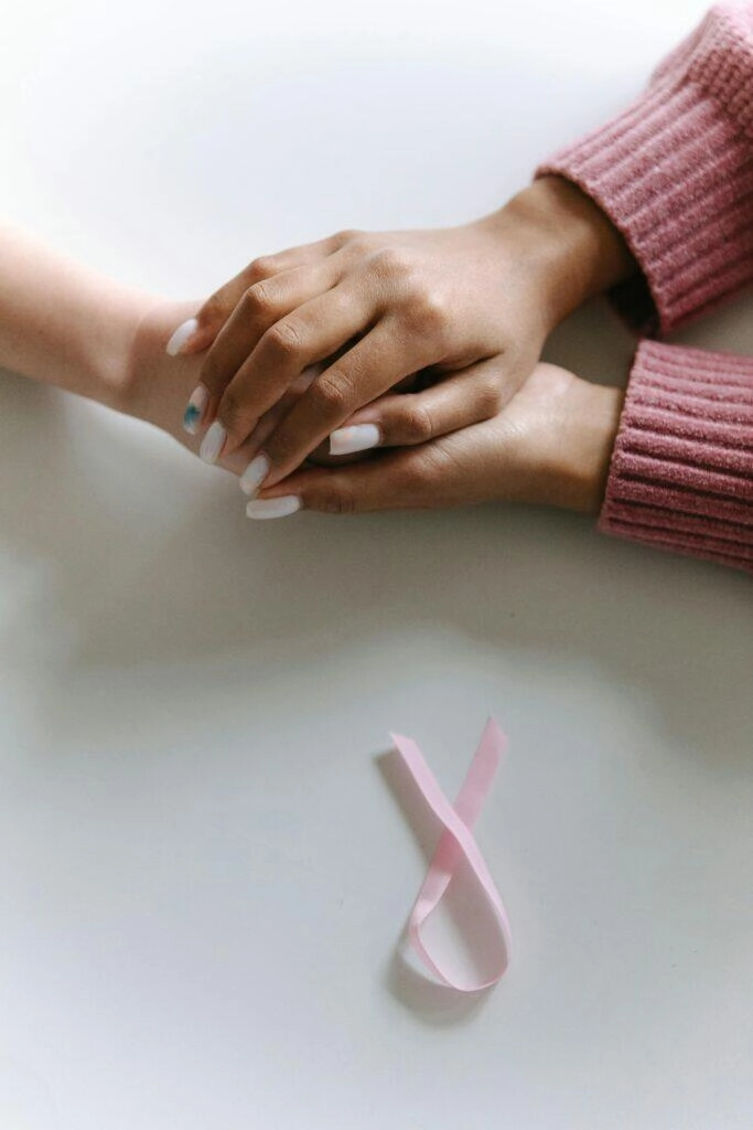 Two hands clasped together, pink ribbon nearby. Supporting cancer charities.