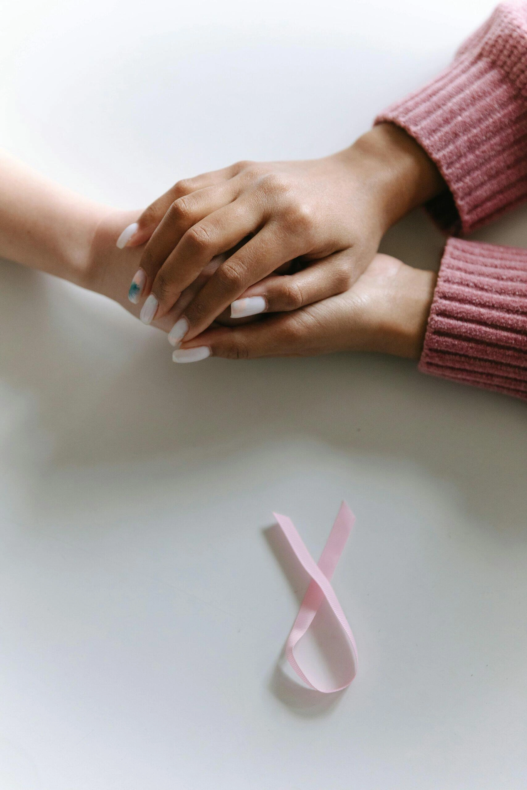 Two hands clasped together, pink ribbon nearby. Supporting cancer charities.