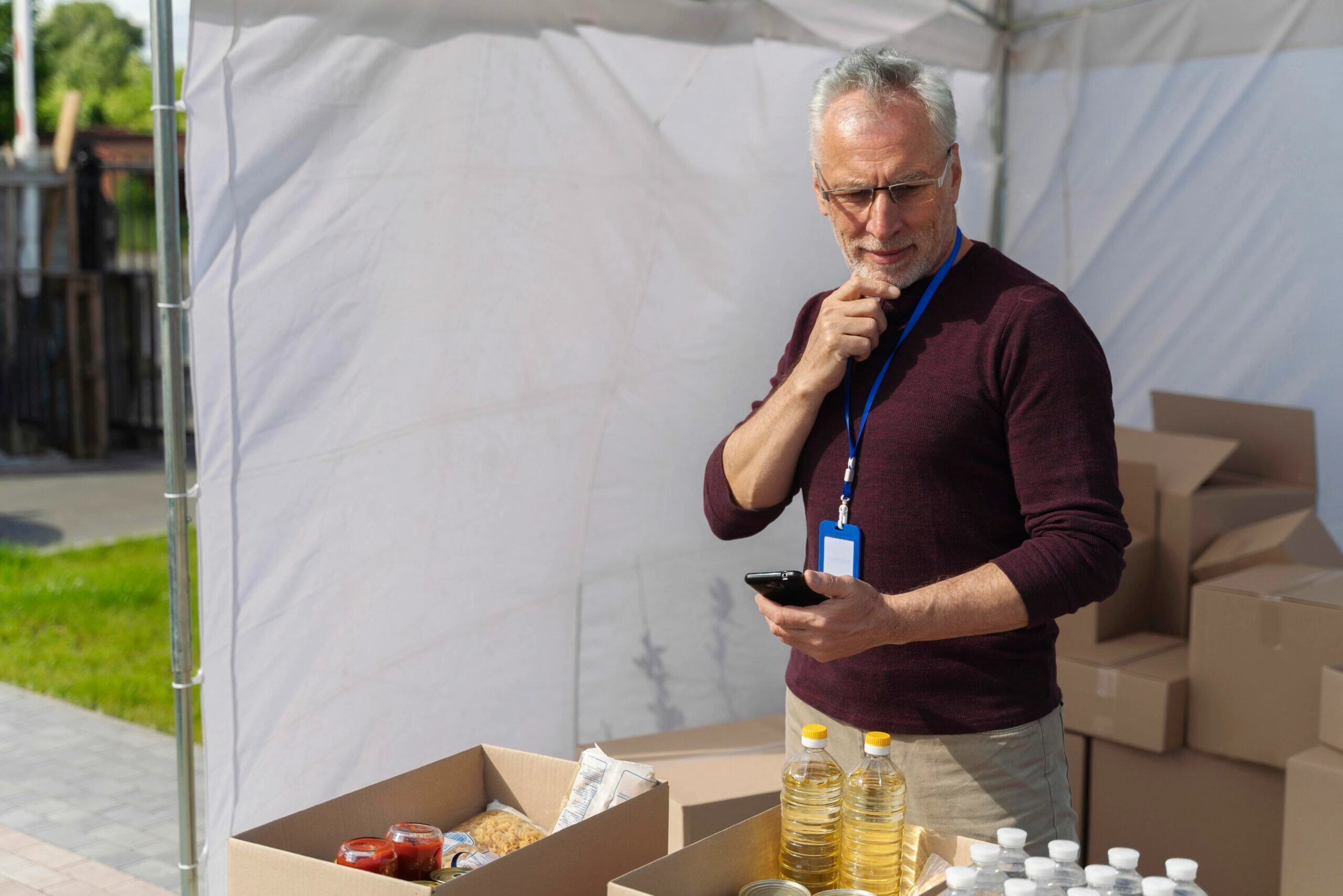 Senior volunteer at a food bank checks inventory on his phone, ensuring ACNC compliance.