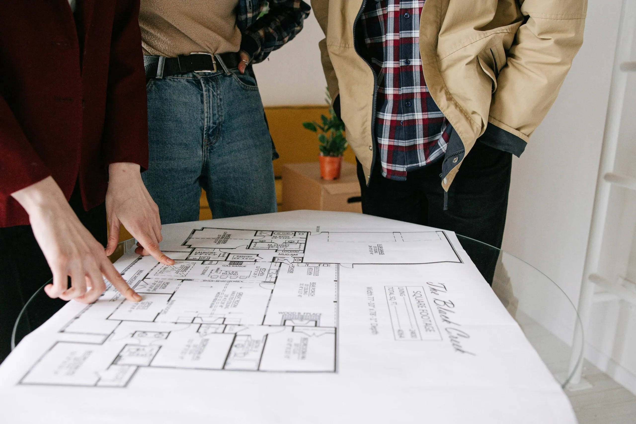 People reviewing architectural blueprints for The Black Creek house plan, discussing land acquisition and development.