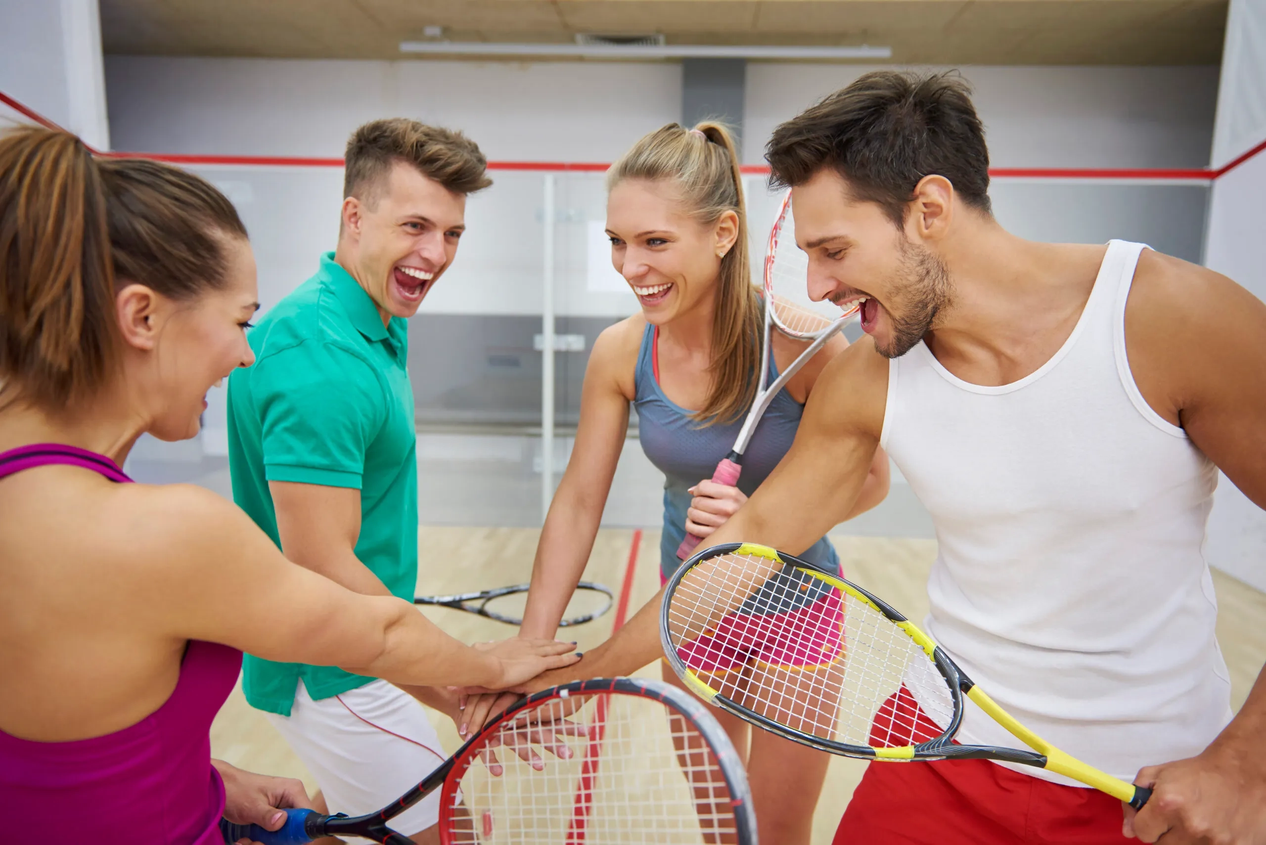 Group of four smiling friends celebrating a squash match win with rackets in hand.