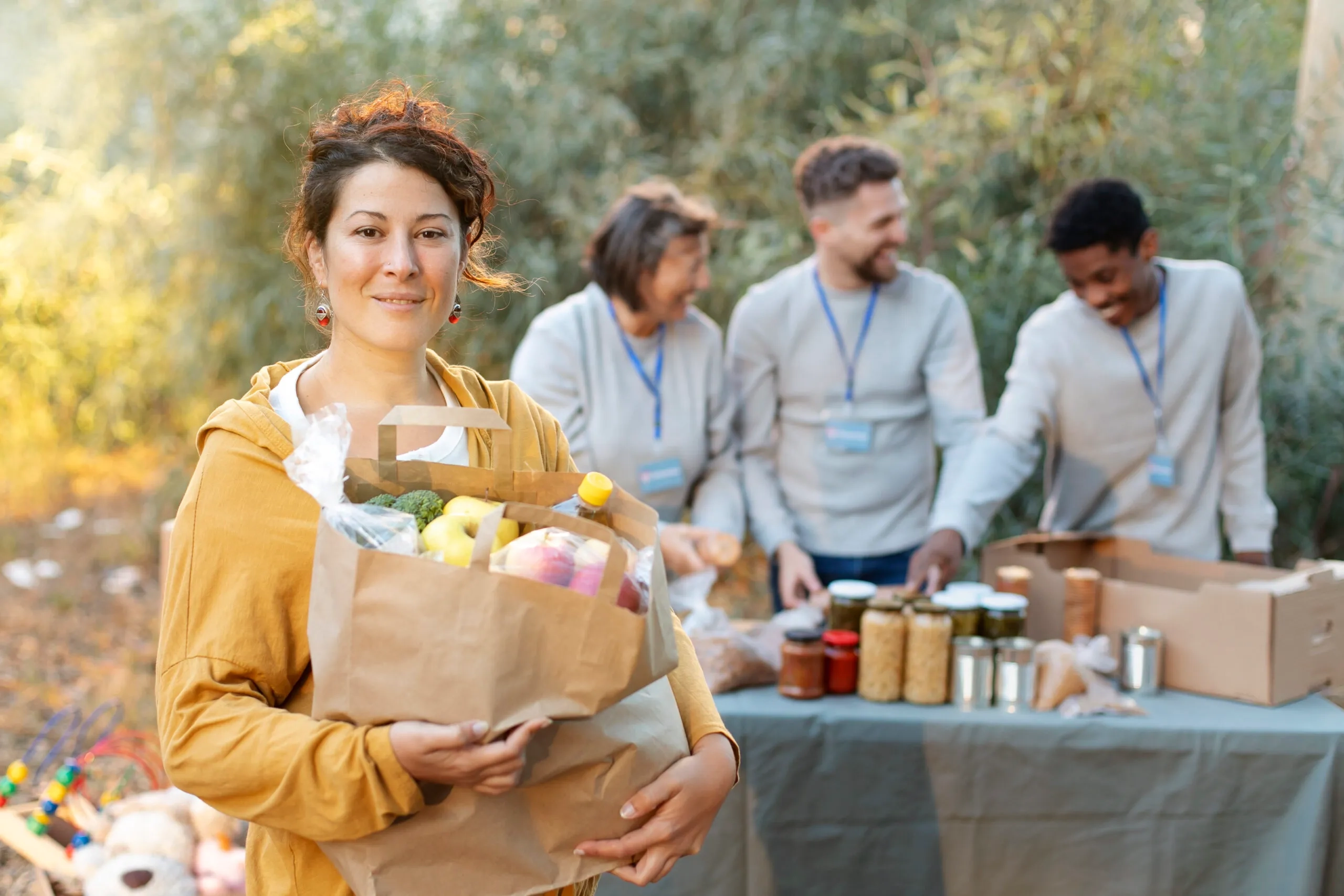 Volunteer holding food donation bag, with other volunteers sorting items behind her.